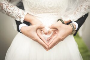 Das Bild zeigt eine Paar bei ihrer Hochzeit, das mit den Händen ein Herz formt.